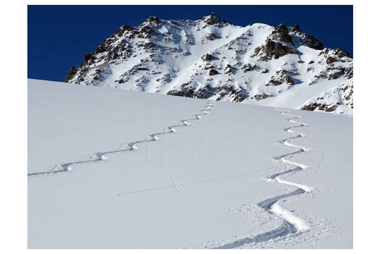 two ski tracks on powder day with mountain on the background