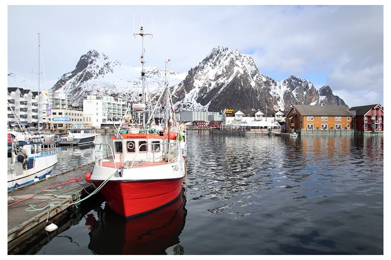 barco pesquero amarrado en pueblo de las islas lofoten. montañas escarpadas en contraste al fondo de la imagen.