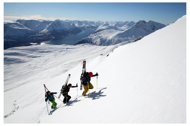trois skieurs avec les skis au dos vers le sommet à Lyngen, Norvège