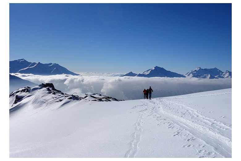 grupo de esquiadores en travesía en el Glaciar du Dôme de Chasseforêt con las montañas italianas al fondo, los picos por encima de la niebla.