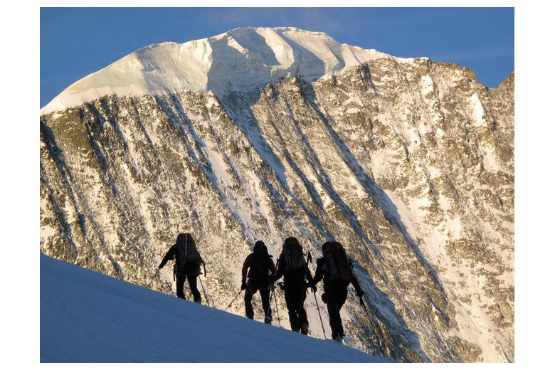 silhouettes des skieurs qui montent vers le sommet avec montagne ensoleillée au fond